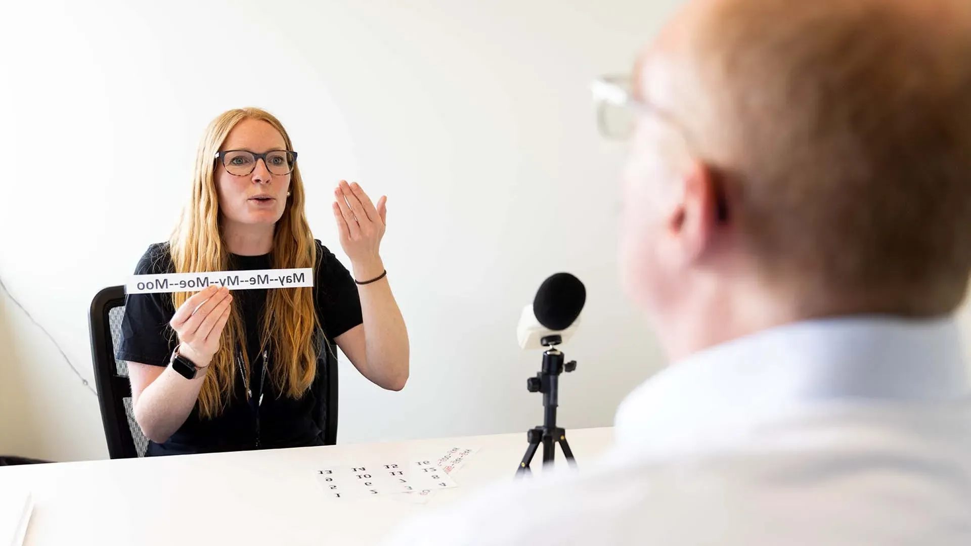 Graduate Clinician working with a client that has Parkinson's Disease. The grad clinician is holding a sign that has 